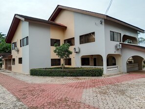 A two-story building with a flat roof, multiple windows, and a small tree in the front yard. - Superb 6-bedroom apartment with AC in Takoradi, best location and beautiful area (Takoradi)