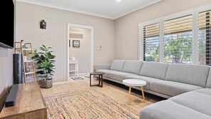A modern living room with a grey sofa, a coffee table, a wooden side table, a patterned rug, and a potted plant. - Tropical Santai Retreat - Pool with separate flat (Toukley)