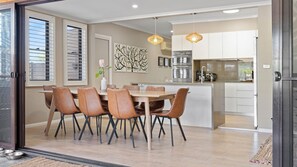 Een eetgedeelte met een houten tafel en lederen stoelen, een keuken met moderne apparatuur, en kunst aan de muur.