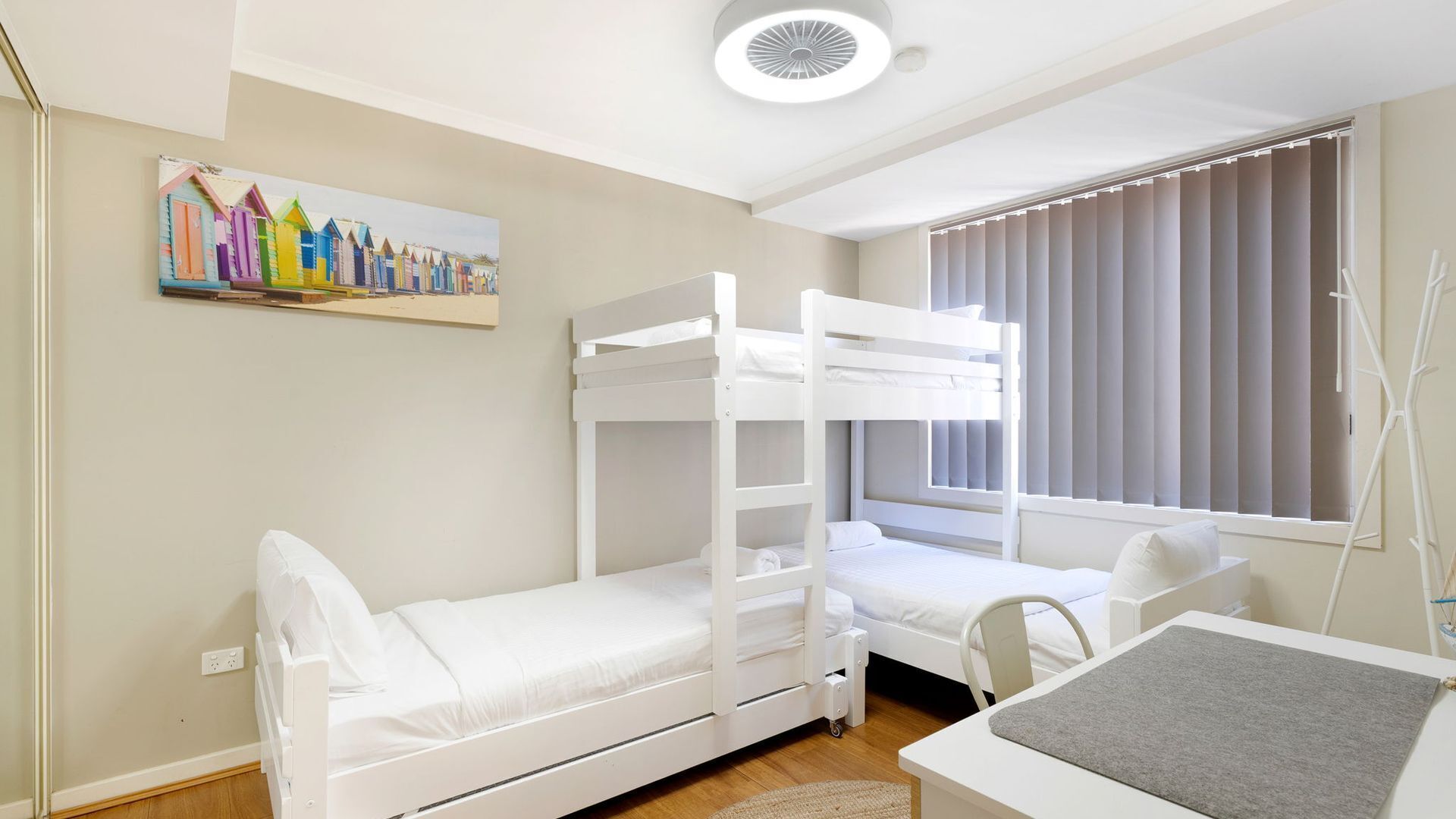 A room with bunk beds, a desk, and a window with blinds.