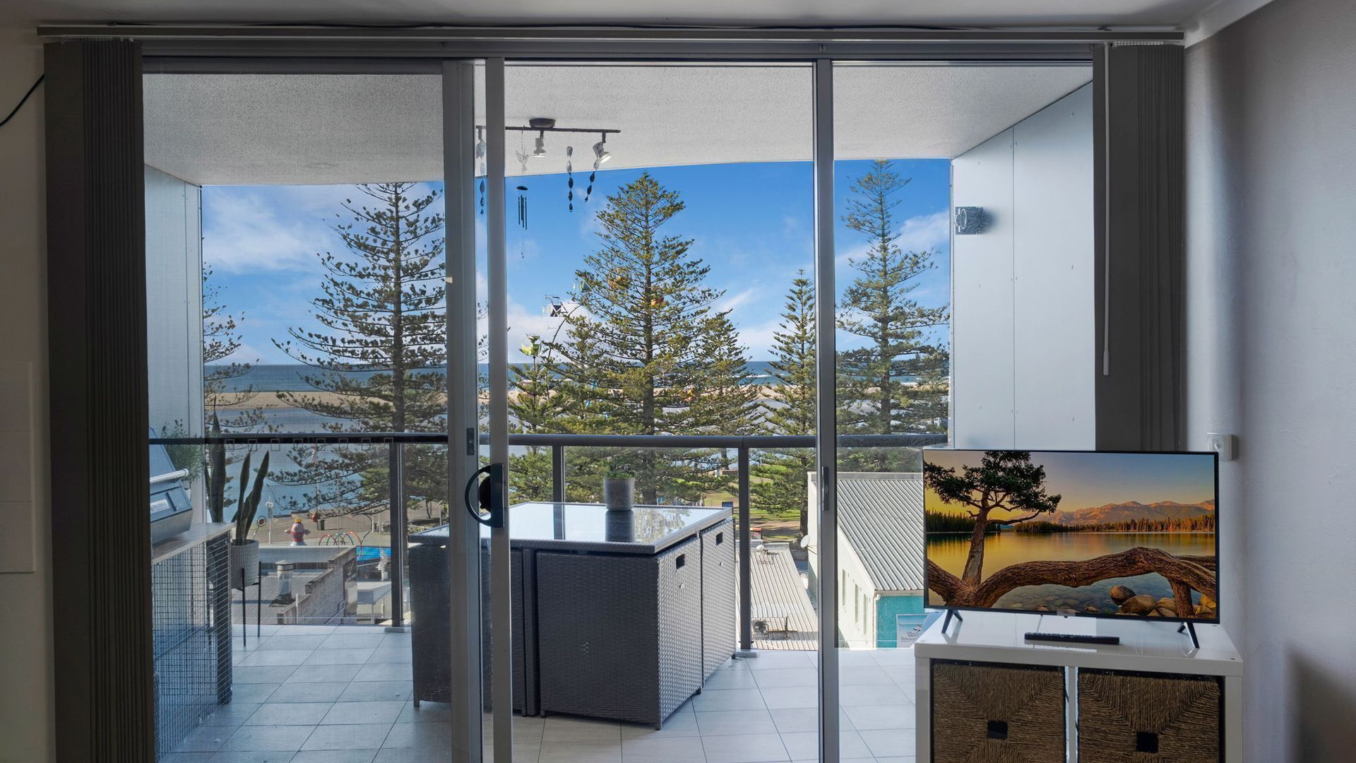 A balcony with a glass door leading to a view of trees and a body of water.