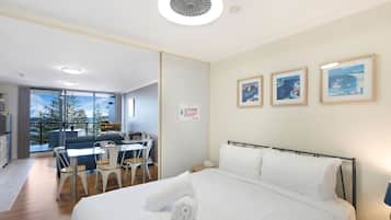 A modern bedroom with a large bed, a dining area with chairs, and a view of the outdoors.