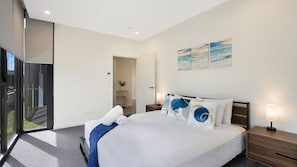 A modern bedroom with a large bed, bedside lamps, a view through a glass door, and a wall with three paintings. - The Accessible Oasis - 3 bedroom disability apartment (The Entrance)