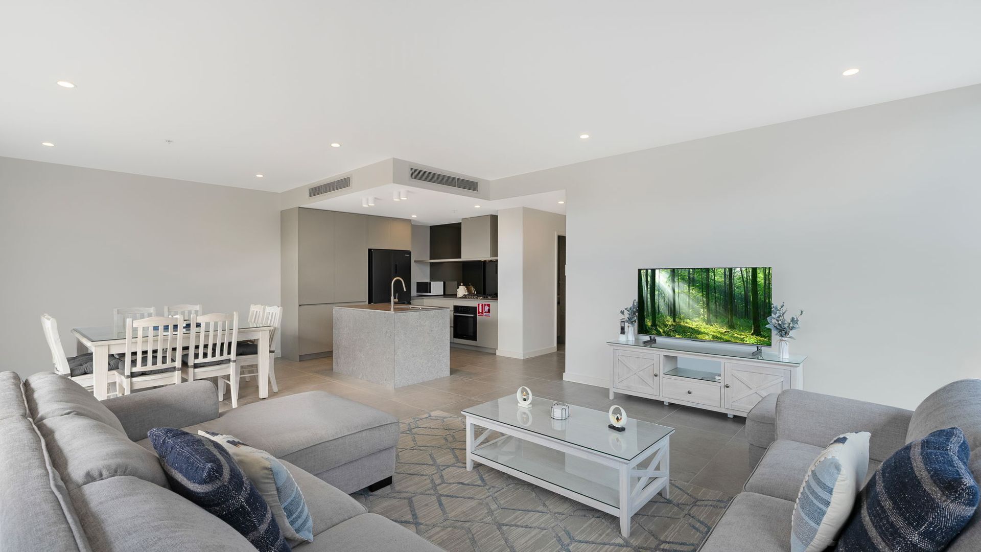 Una sala moderna con sofá, mesa de centro y televisor mostrando un paisaje forestal.