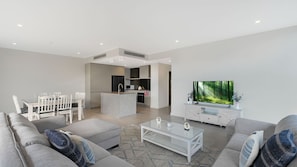 A modern living room with a sofa, coffee table, and a television displaying a forest scene. - The Accessible Oasis - 3 bedroom disability apartment (The Entrance)