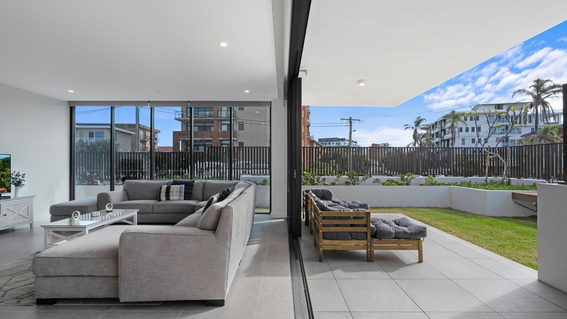 A modern living room with a grey sofa, a wooden bench, and a glass wall offering a view of the cityscape.