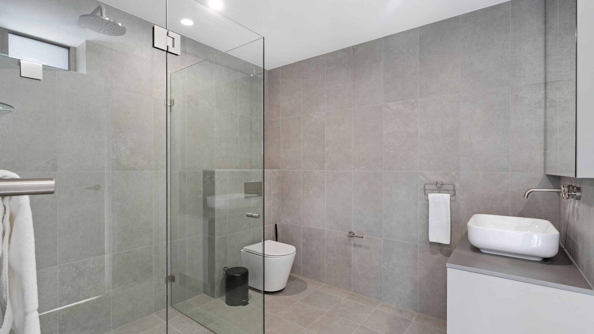 Et moderne badeværelse med en glasbrusekabine, toilet og håndvask.