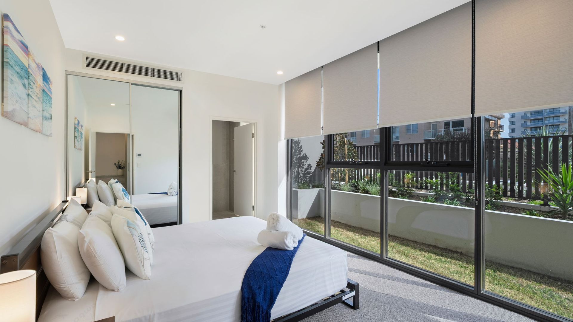 Ein modernes Schlafzimmer mit einem großen Bett, einem Nachttisch und einem Fenster mit Blick auf einen Innenhof.