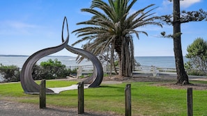 A metal sculpture, a grassy area, a palm tree, and a view of the water. - The Accessible Oasis - 3 bedroom disability apartment (The Entrance)
