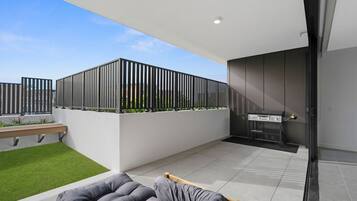 Eine moderne Terrassenanlage im Freien mit Grill, Sitzbank und kleinem Gartenbereich.