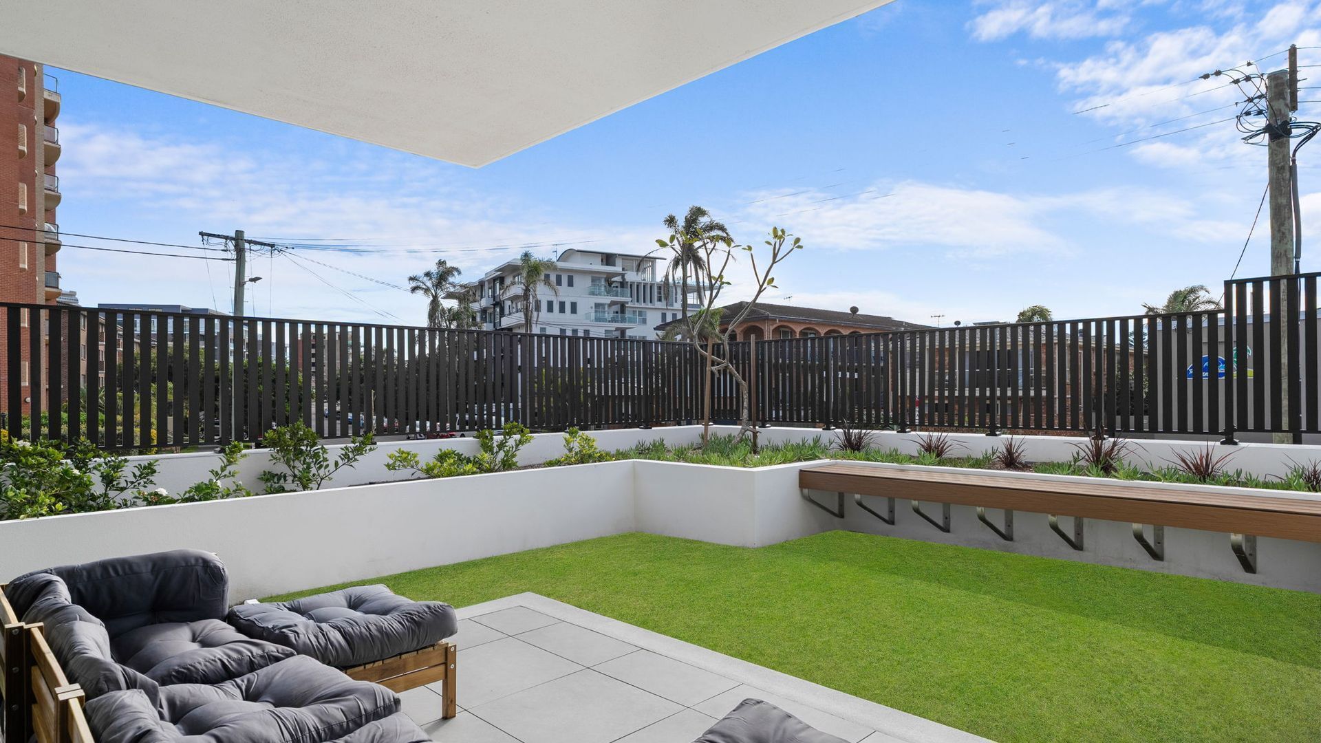 Une terrasse avec un revêtement de gazon synthétique, un banc en bois et un espace salon agrémenté de coussins.