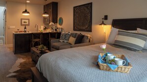 A cozy bedroom with a large bed, a small desk, and a dining area. - 4 Suites + Balconies | Steps to DT Square | Paso Park Suites Buyout (Paso Robles)