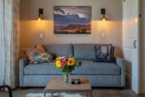 Ein Wohnzimmer mit grauem Sofa, einem Holztisch mit Blumenvase und zwei Wandlampen.