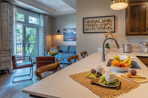 A modern kitchen with a central island, a dining area with chairs, a sofa, and a view of the outdoors. - 4 Suites + Balconies | Steps to DT Square | Paso Park Suites Buyout (Paso Robles)