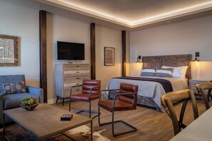 Een moderne slaapkamer met een bed, twee leren fauteuils, een klein tafeltje, een dressoir en een televisie.