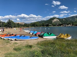A lakeside area with boats lined up on the shore, a sandy beach, and mountains in the background. - Charming Rustic Avon Mountain Condo; near lift (Avon)