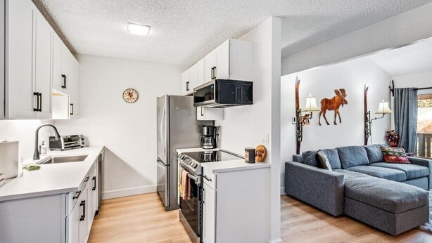 A compact kitchen with modern appliances, a dining area with a table and chairs, and a living room with a sofa and a mounted television. - Charming Rustic Avon Mountain Condo; near lift (Avon)