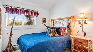 A bedroom with a bed, a window with curtains, a lamp, and a wall-mounted picture. - Charming Rustic Avon Mountain Condo; near lift (Avon)