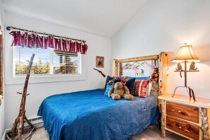 Ein Schlafzimmer mit einem Bett, einem Fenster mit Vorhängen, einer Lampe und einem Wandbild.