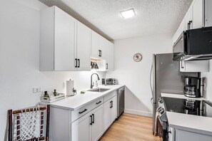 A modern kitchen with white cabinetry, a stainless steel refrigerator, a coffee machine, and a clock on the wall. - Charming Rustic Avon Mountain Condo; near lift (Avon)