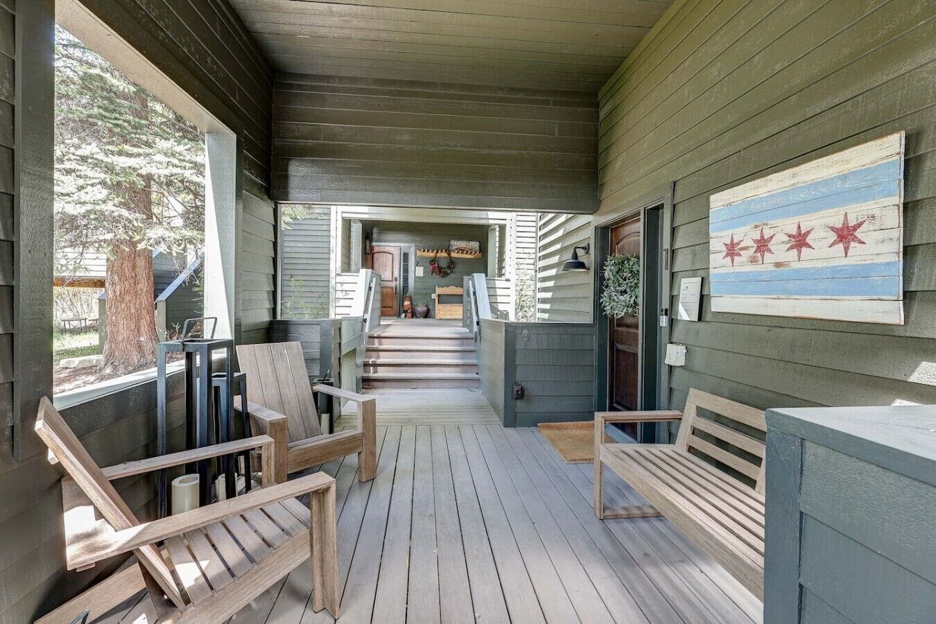 Eine Holzterrasse mit Stühlen und einer Bank, die zu einer überdachten Veranda mit Blick auf ein Haus führt.