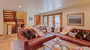 A spacious living room with a large leather sofa, wooden coffee table, and a staircase leading to an upper level.