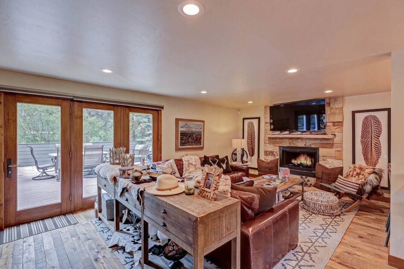 A spacious living room with a fireplace, comfortable seating, and a view through large glass doors to an outdoor deck.