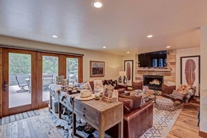 A spacious living room with a fireplace, comfortable seating, and a view through large glass doors to an outdoor deck.