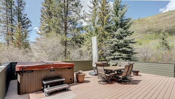 An outdoor deck with a barbecue grill, a table with chairs, and a potted plant.
