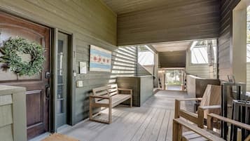 Een houten veranda met een bank, een deur versierd met een krans, en een lijst met een foto aan de muur.