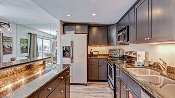 Une cuisine moderne avec des meubles de couleur sombre, des plans de travail en granit, un réfrigérateur, un four à micro-ondes et un grille-pain.