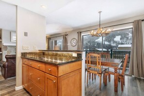 A kitchen with a granite countertop and wooden cabinets, a dining area with a table and chairs, and a large window with a view of a snowy landscape.