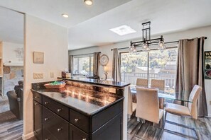 A modern kitchen with a large island, dining area with chairs, and a view of the outdoors. - Lionshead 2BR - Views, Walk to Gondola & Hot Tubs (Vail)