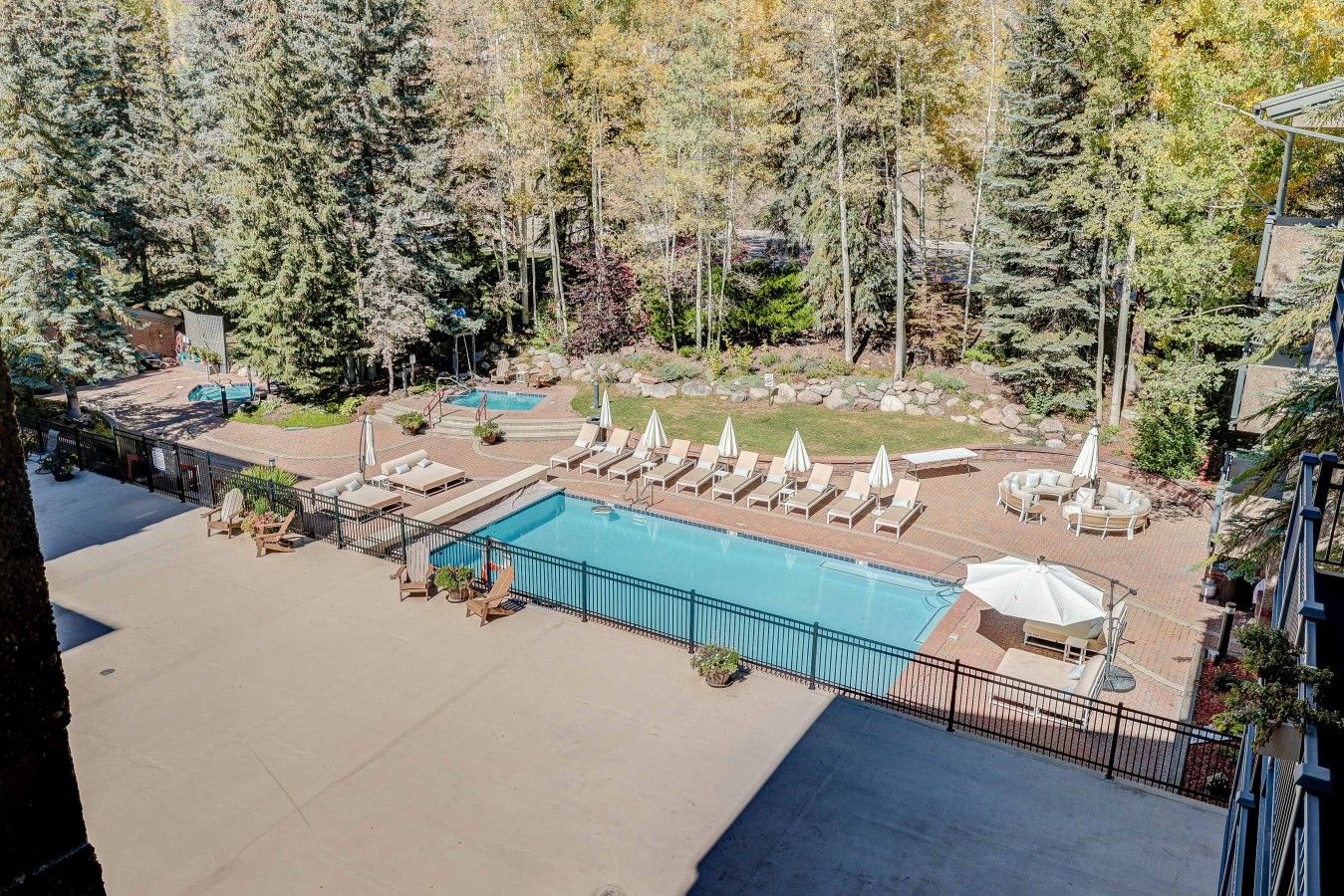 Un espace piscine doté de plusieurs chaises longues et de parasols, entouré d’arbres et agrémenté d’une terrasse en briques.