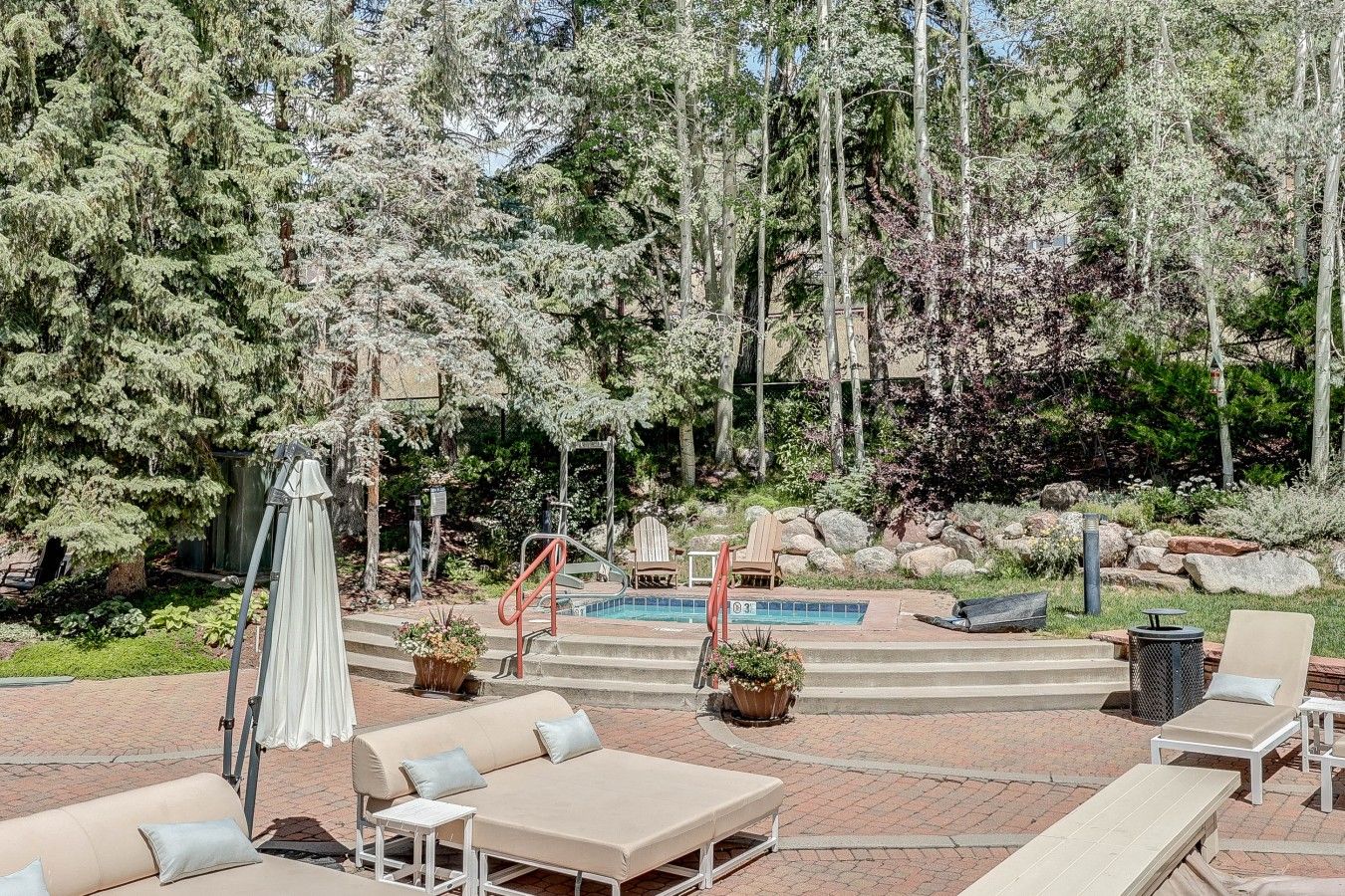 A poolside area with outdoor seating, a pool, and a natural backdrop of trees and shrubs.