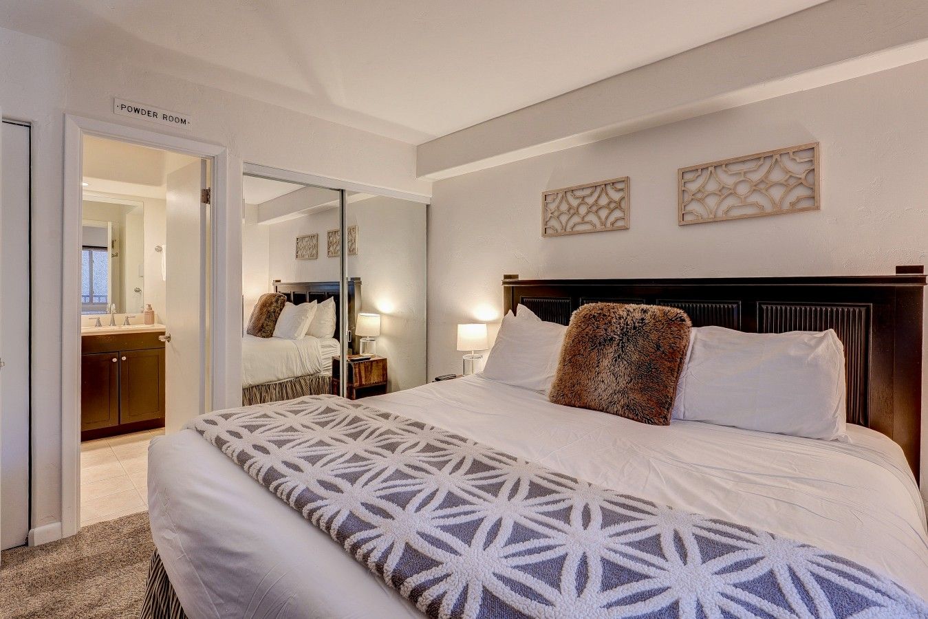 Habitación de hotel con cama, mesitas de noche, un espejo y una puerta que da al baño de cortesía.