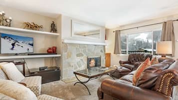 Una sala acogedora con chimenea de piedra, sofá de cuero y un televisor en un estante.