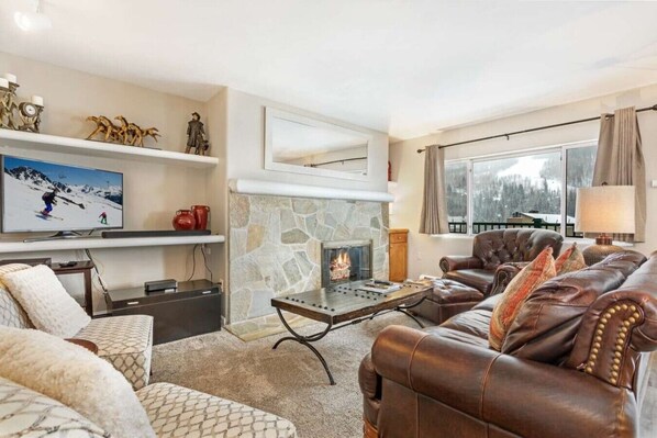 A cozy living room with a stone fireplace, leather sofa, and a television on a shelf.