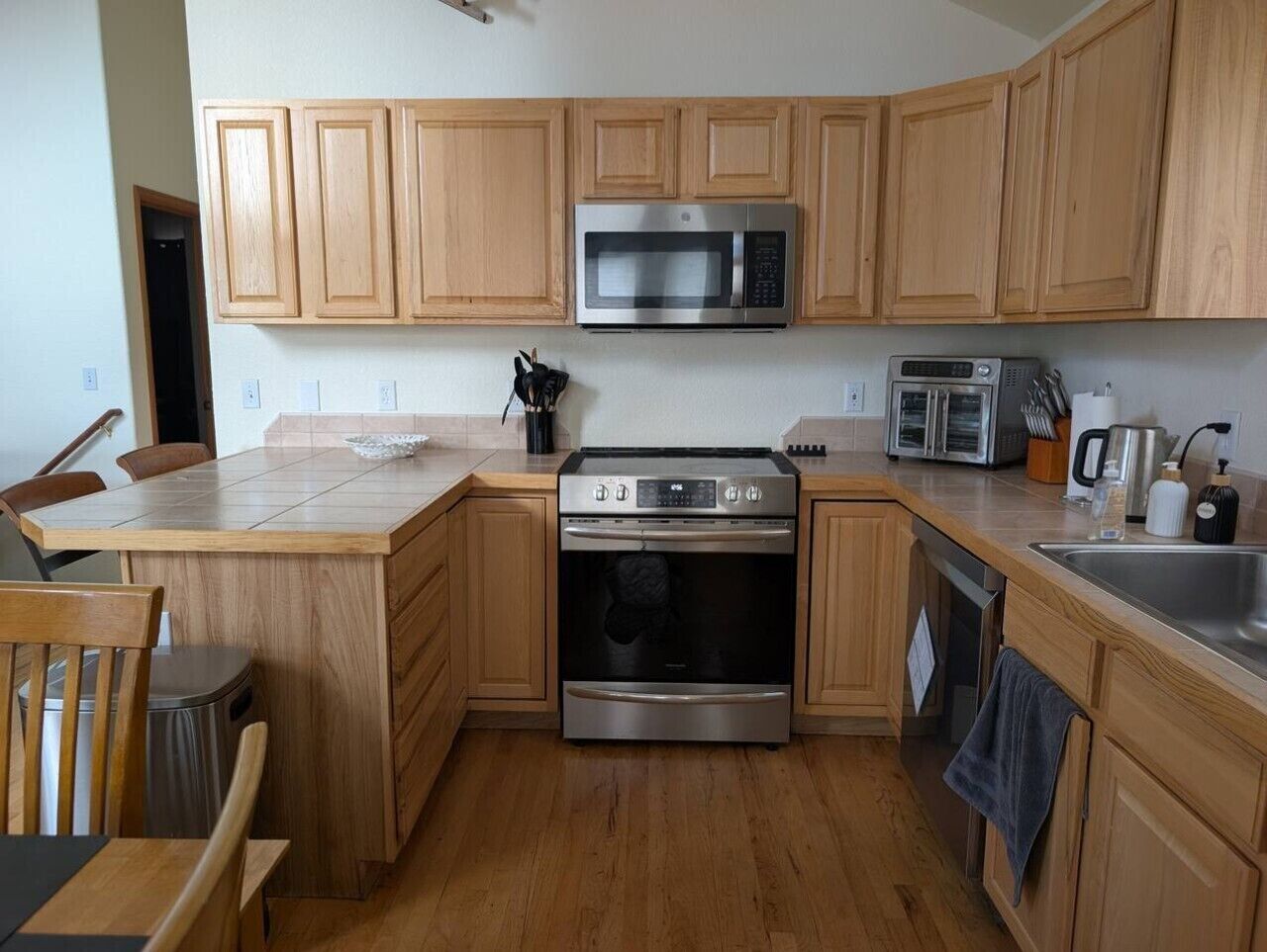 A kitchen with wooden cabinets, stainless steel appliances including a microwave, oven, and toaster, and a dining area with a table and chairs.