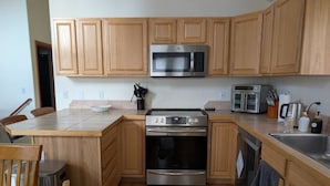Eine Küche mit Holzausstattung, Edelstahlgeräten – darunter Mikrowelle, Backofen und Toaster – sowie ein Essbereich mit Tisch und Stühlen.