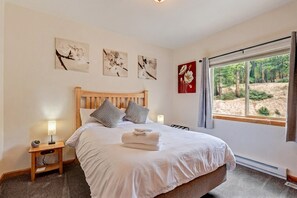 Ein Schlafzimmer mit einem hölzernen Bett, zwei Nachttischen mit Lampen, einem Fenster mit Blick auf Bäume und floralen Wandbildern.