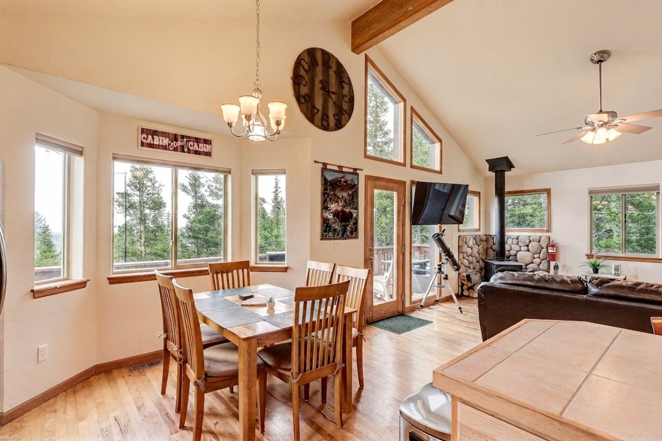 A spacious living area with a dining table, chairs, a fireplace, a television, and large windows offering views of the outdoors.