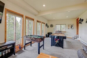 Um quarto espaçoso com mesa de pebolim, mesa de bilhar e grandes janelas com vista para árvores.