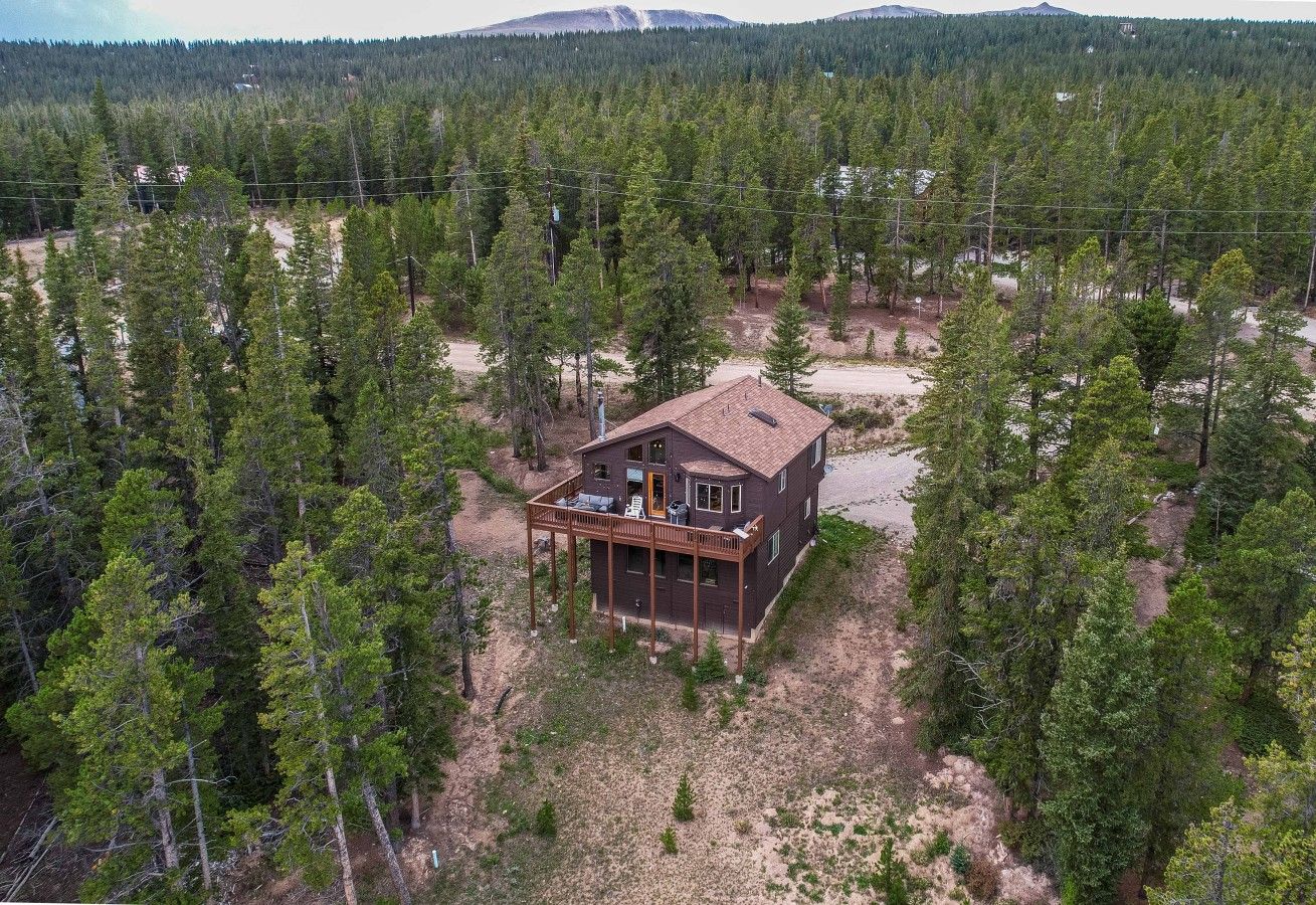 A two-story house with a deck, surrounded by dense forest.