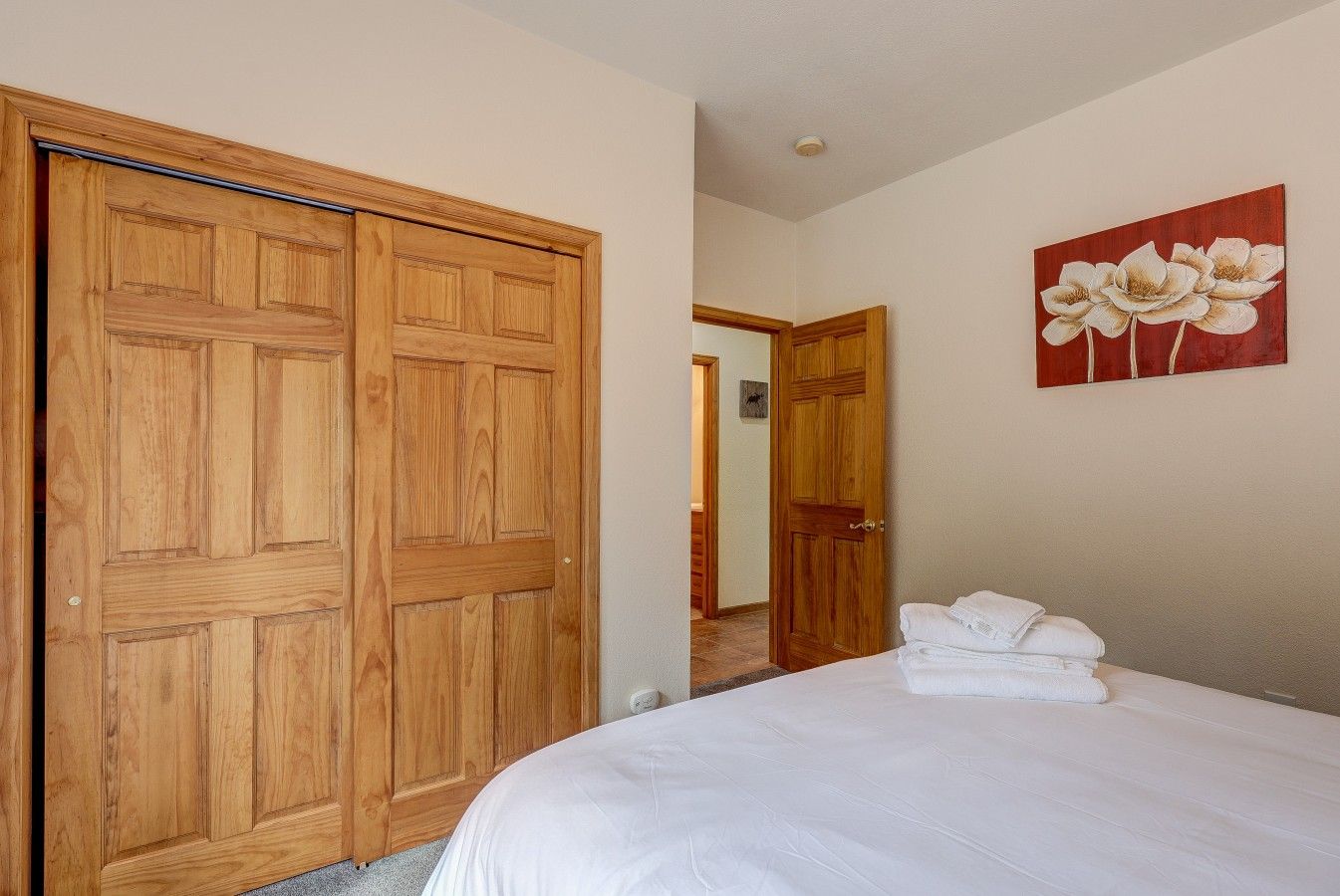 A bedroom with a large wooden wardrobe, a bed with white bedding, and a floral painting on the wall.