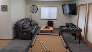 Ein Wohnzimmer mit Billardtisch, einer Ledersofa, einem Couchtisch, einem Fernseher und einem Kicker.
