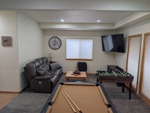 A living room with a pool table, a leather sofa, a coffee table, a television, and a foosball table. - Mountain View Retreat | Game Room & Fireplace (Fairplay)