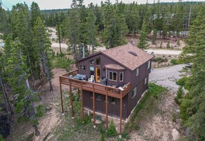 Eine zweistöckige Holzhütte mit einer Terrasse, umgeben von einem Wald.