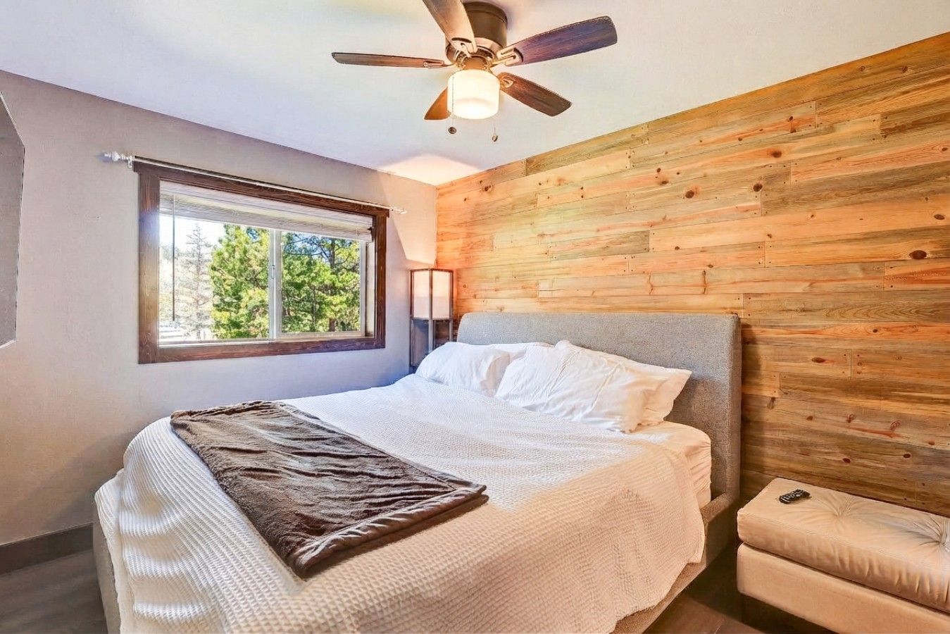 A bedroom with a bed, a ceiling fan, a window, and a wooden wall.