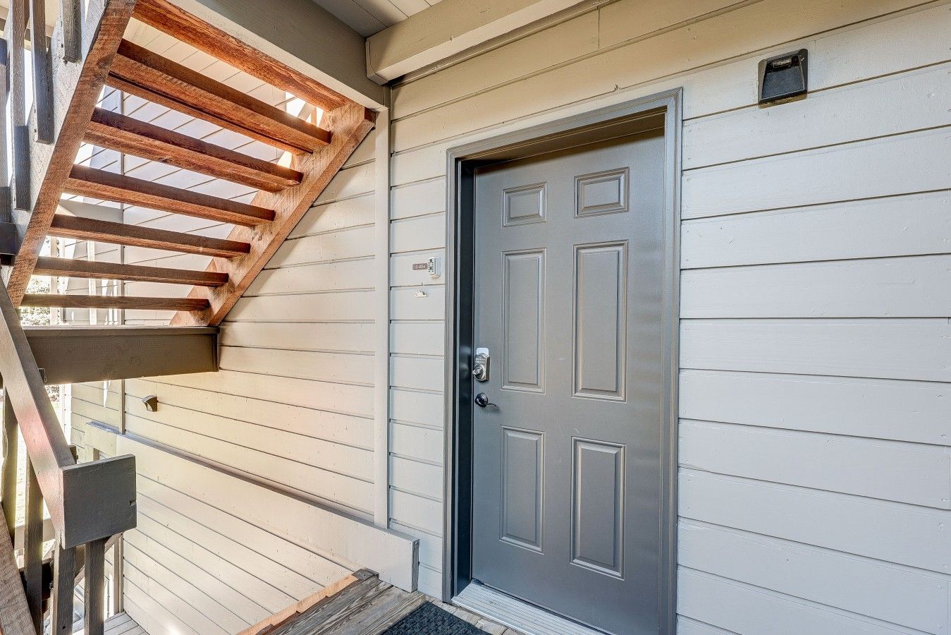 Une maison avec une porte grise, un porche en bois et une petite boîte aux lettres.